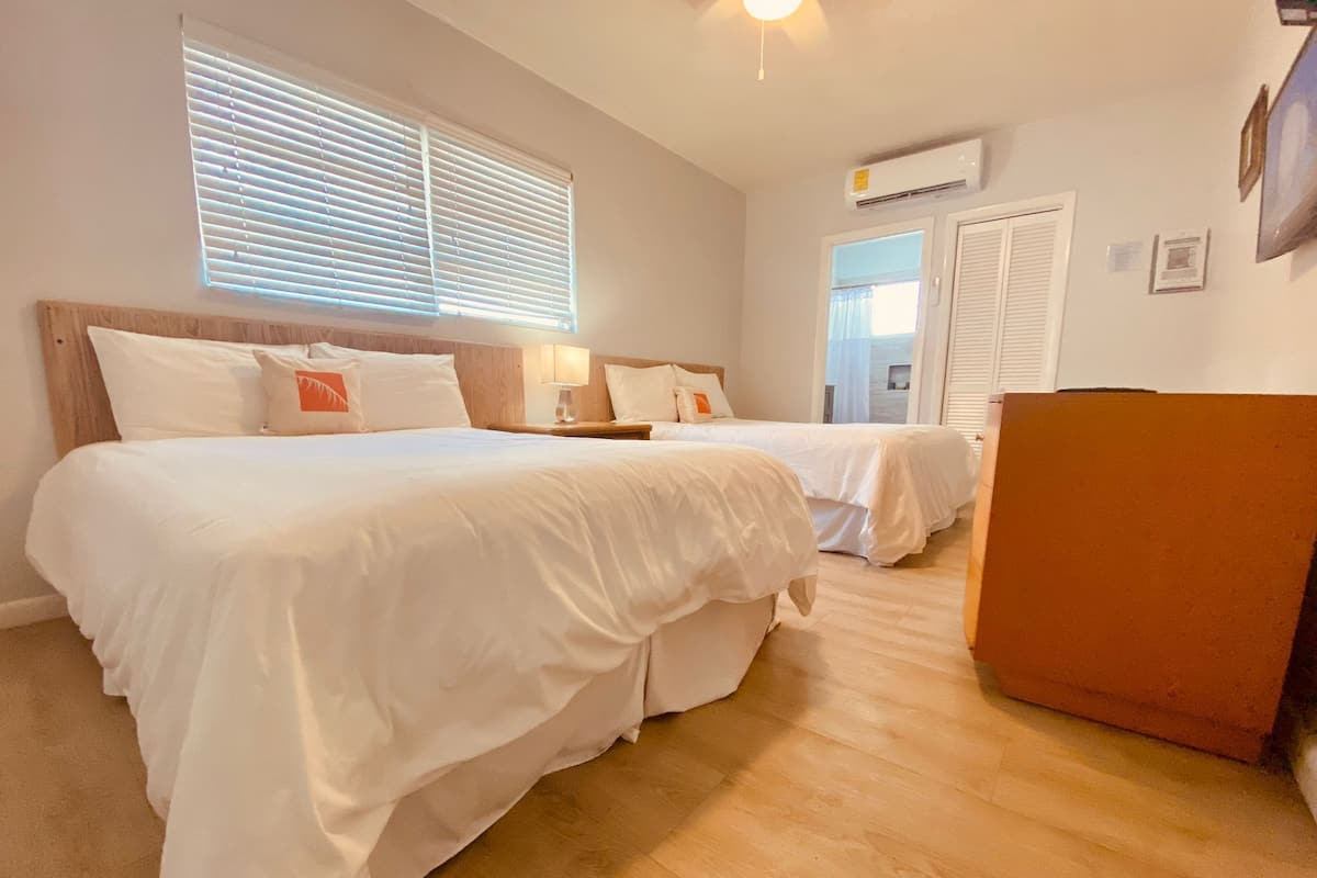 A hotel room with two beds, a wooden headboard, a nightstand, a desk, and an air conditioning unit.