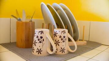 Un espacio de cocina con un organizador de utensilios de madera, dos tazas con motivos florales y una pila de platos en una bandeja.