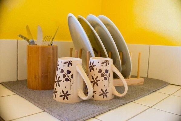 Un espacio de cocina con un organizador de utensilios de madera, dos tazas con motivos florales y una pila de platos en una bandeja.