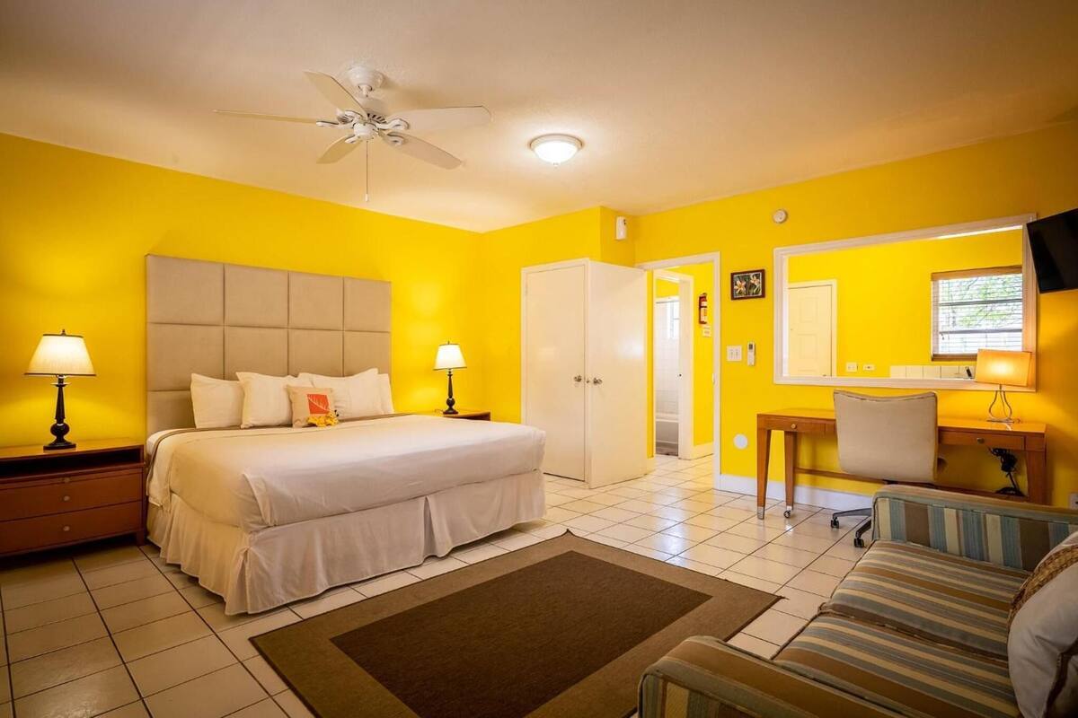 A hotel room with a bed, bedside tables, a ceiling fan, a TV, a desk, and a chair.