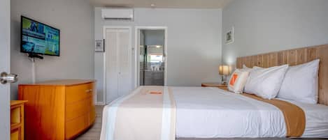 A hotel room with a bed, a wooden dresser, a TV mounted on the wall, and a ceiling fan.