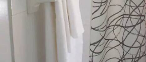 A bathroom with a white tiled wall, a metal towel rack with two white towels, and a shower curtain with a black abstract pattern.