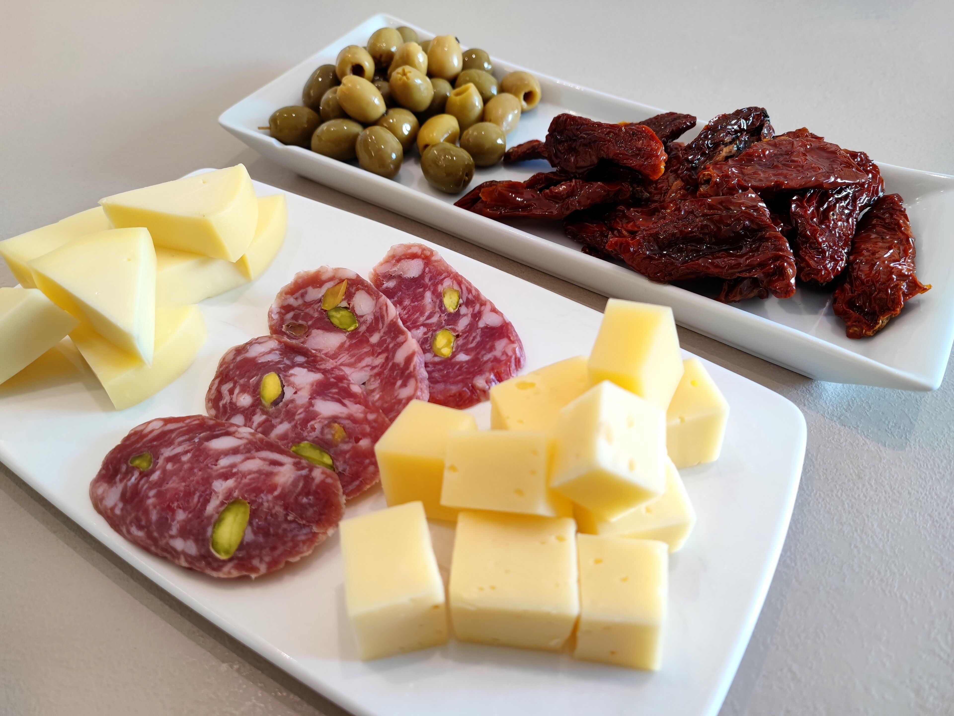A plate with various cheeses, salami, olives, and dried peppers.