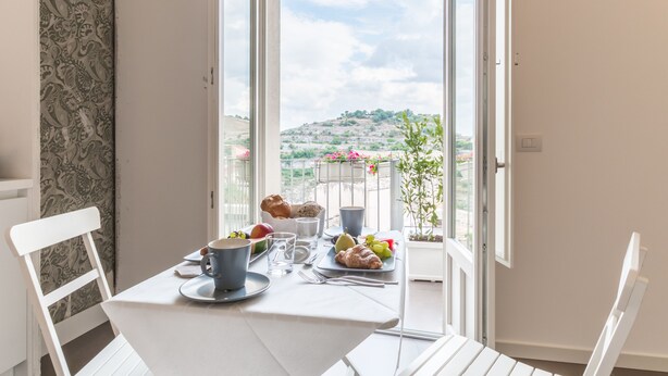 Un balcón con una mesa dispuesta para el desayuno, que incluye croissants, frutas y una taza.