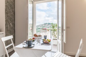 Un balcón con una mesa dispuesta para el desayuno, que incluye croissants, frutas y una taza.