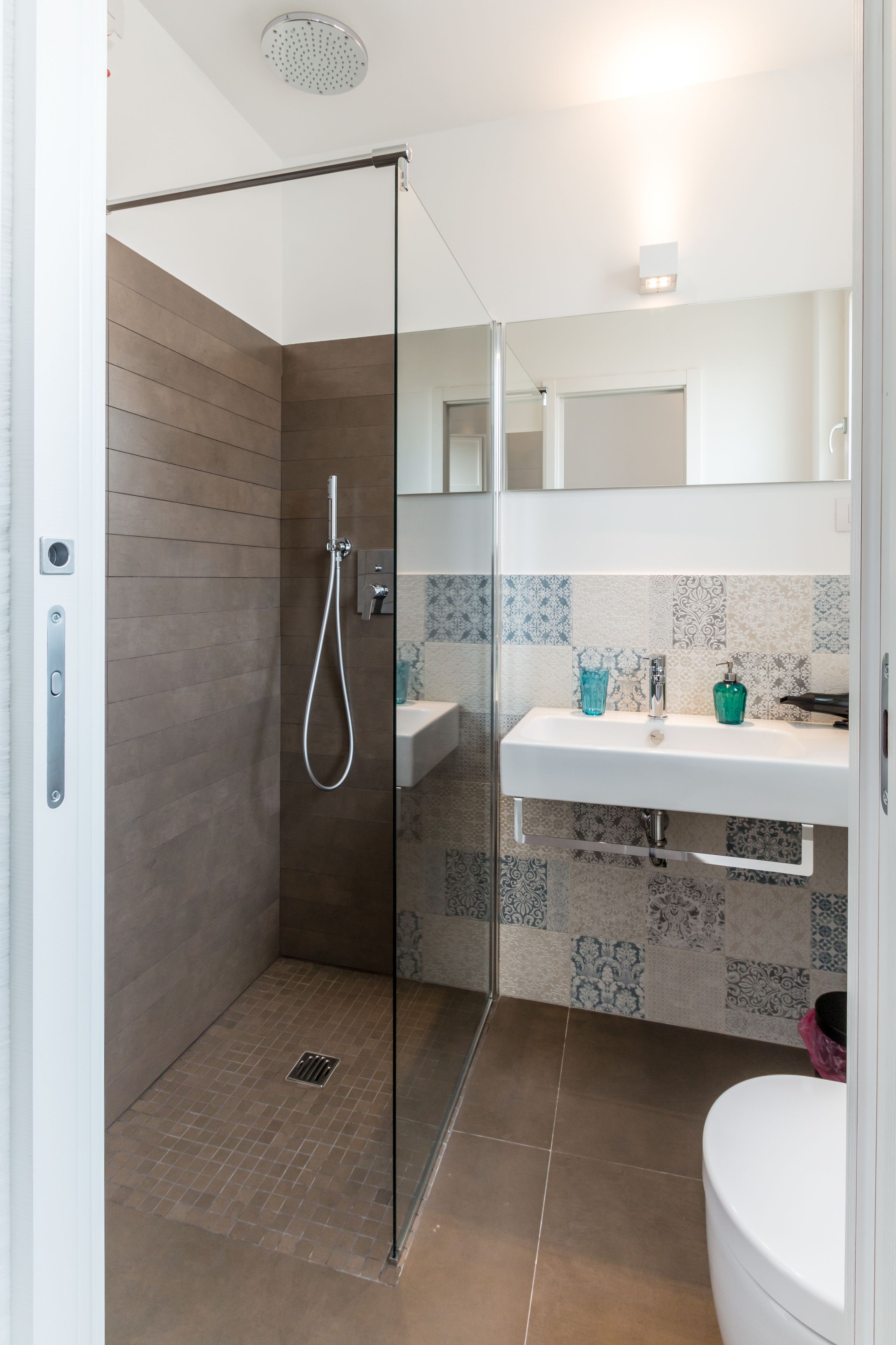 Een moderne badkamer met een douchecabine van glas, een witte wastafel en een betegelde spatwand.