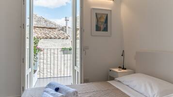 Un dormitorio con una cama, una mesita de noche, una lámpara, un cuadro en la pared y vistas a un patio a través de una puerta abierta.