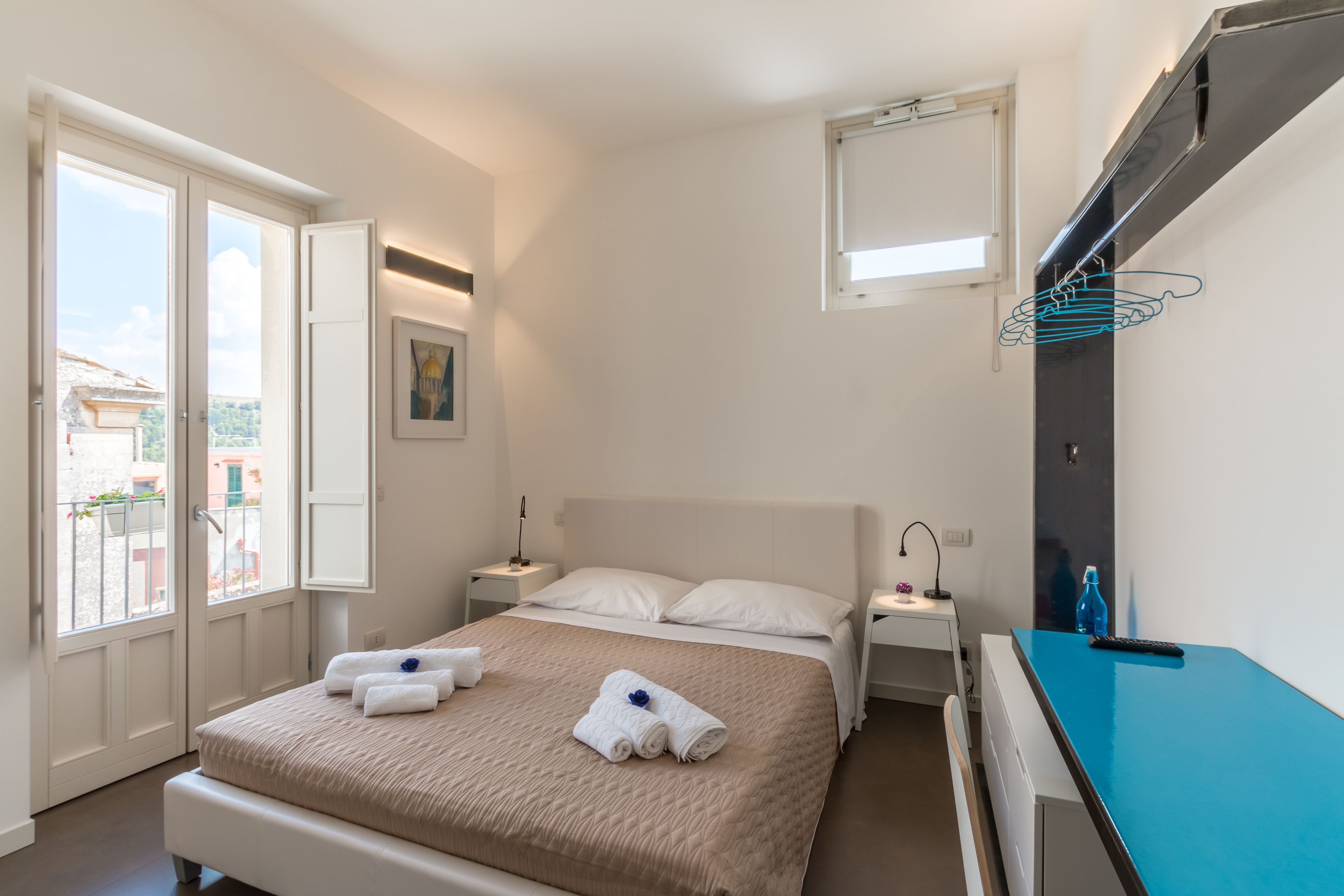 A bedroom with a bed, nightstands, a desk, and a view of the outside.