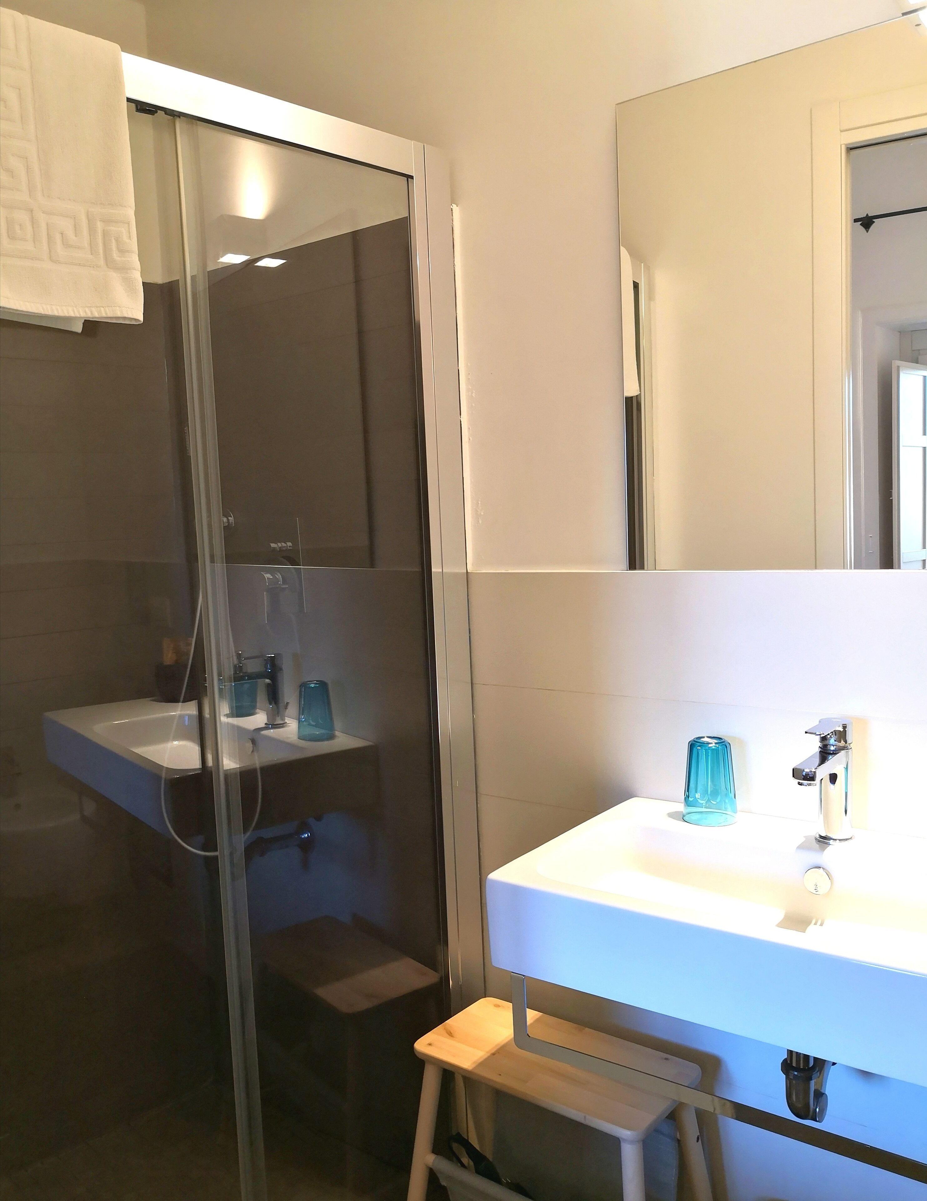 A bathroom with a glass-enclosed shower, a white sink with a blue glass container, and a mirror above the sink.