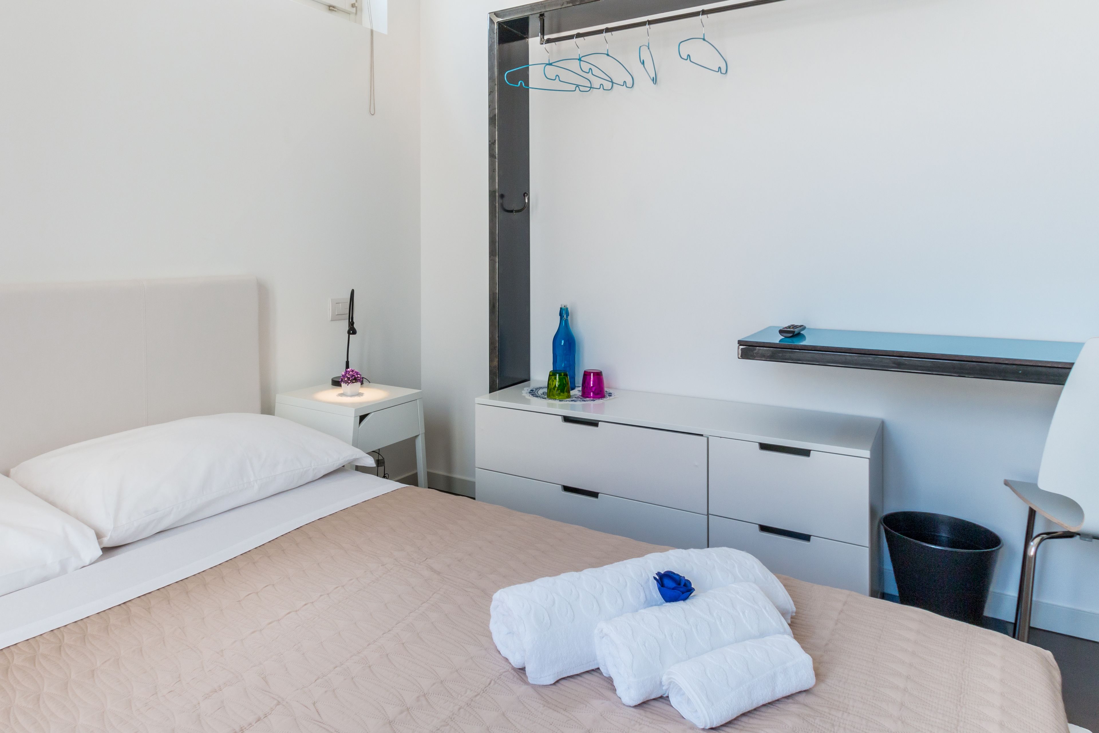 A hotel room with a bed, a bedside table, a mirror, a shelf with toiletries, and a chair.