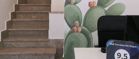 Een hotelinterieur met een trap, een wanddecoratie van een cactus en een bureau waarop een plaquette voor een gastbeoordelingsprijs staat.