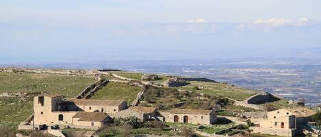 A rural village with stone buildings, terraced fields, and a distant view of the countryside.