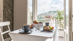 Comedor con una mesa preparada para el desayuno, vistas al exterior y un balcón con plantas.