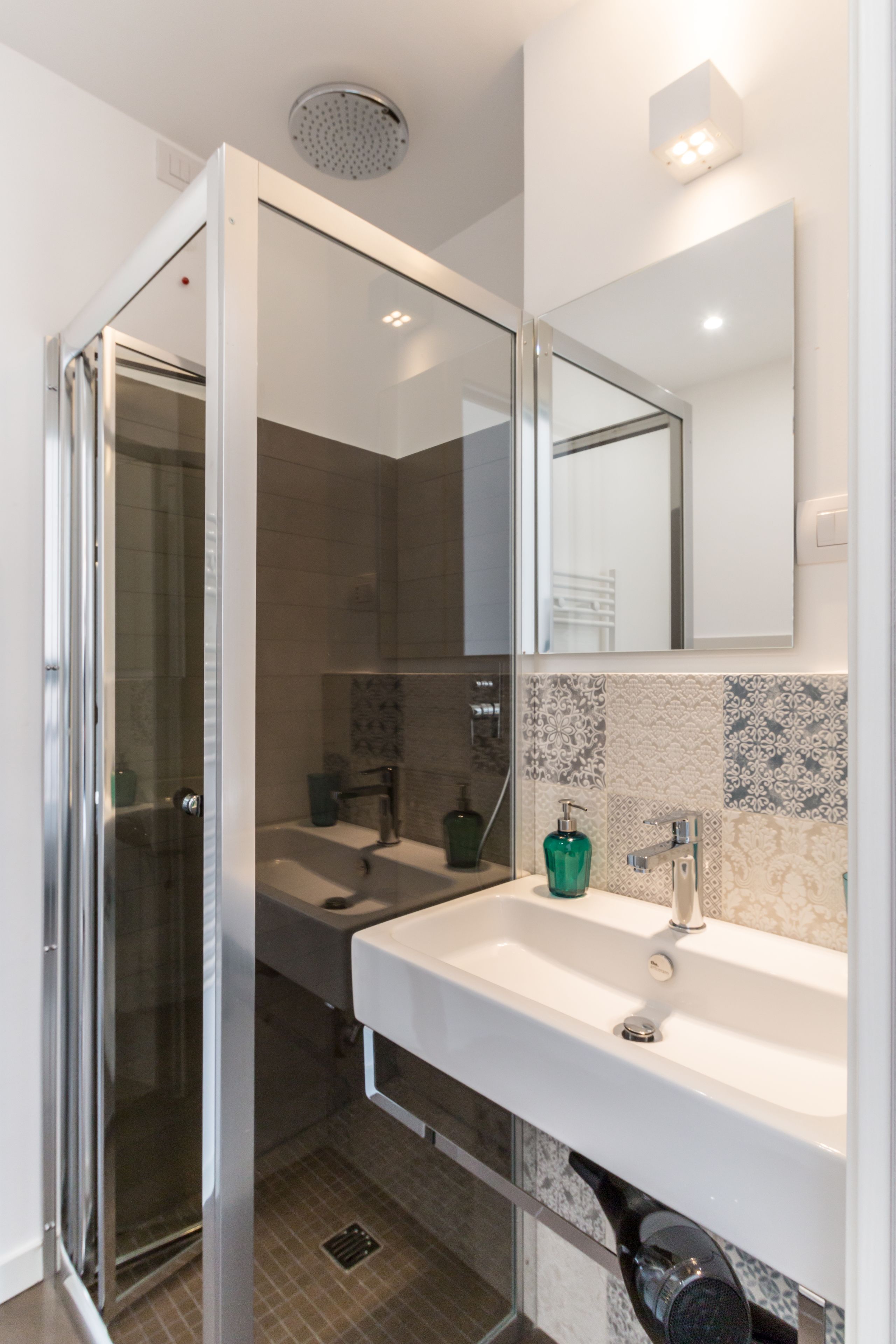 A modern bathroom with a glass shower enclosure, a white sink, and a mirror above it.