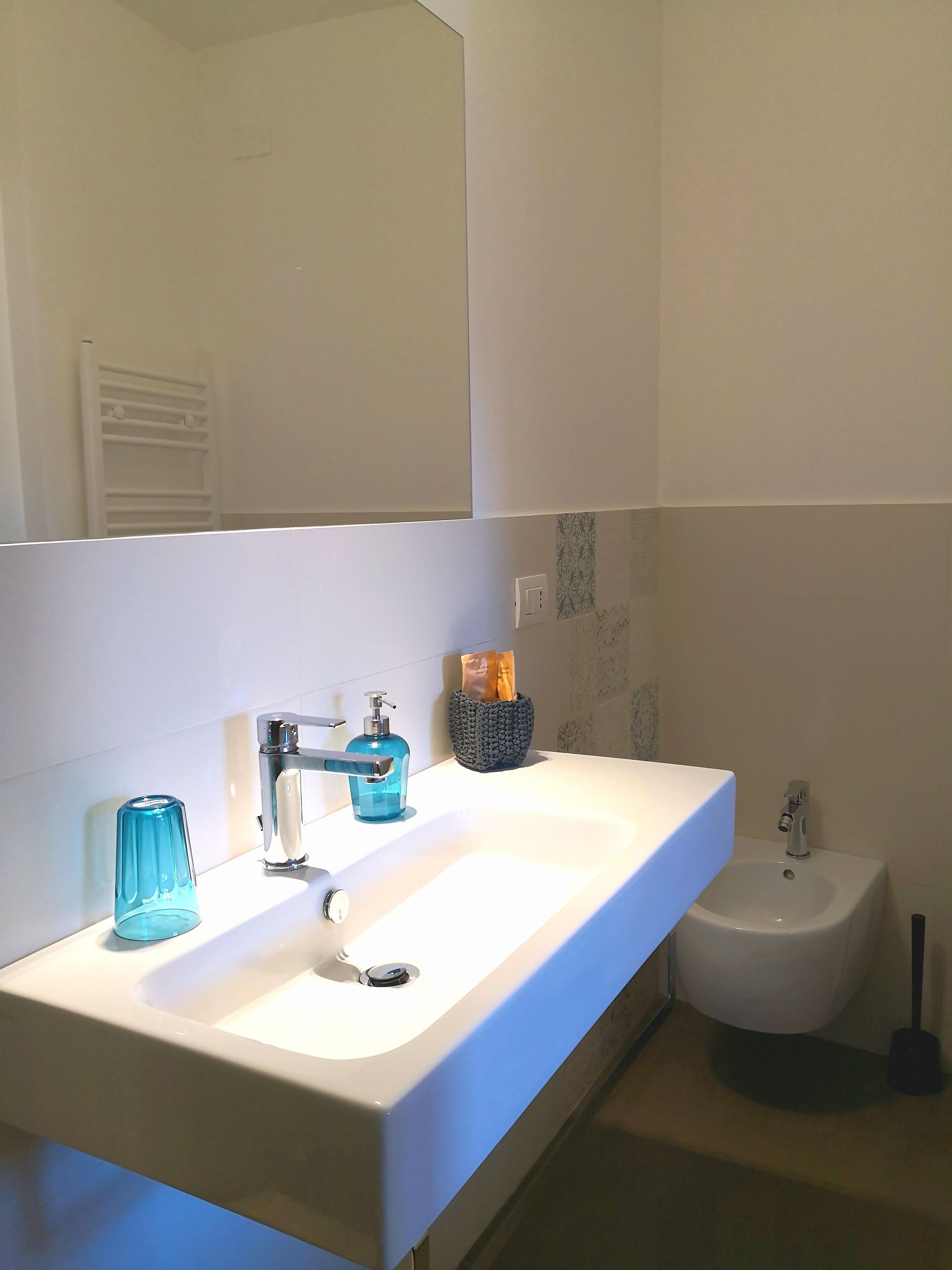 A bathroom with a white sink, a blue glass soap dispenser, and a bidet.