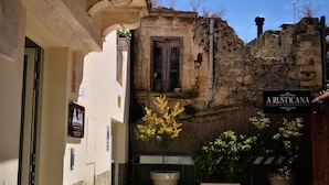 Un patio con pavimento de piedra, plantas en macetas, un edificio rústico con pared de piedra y un letrero que dice 'A Rusticana Cucina Casereccio'.