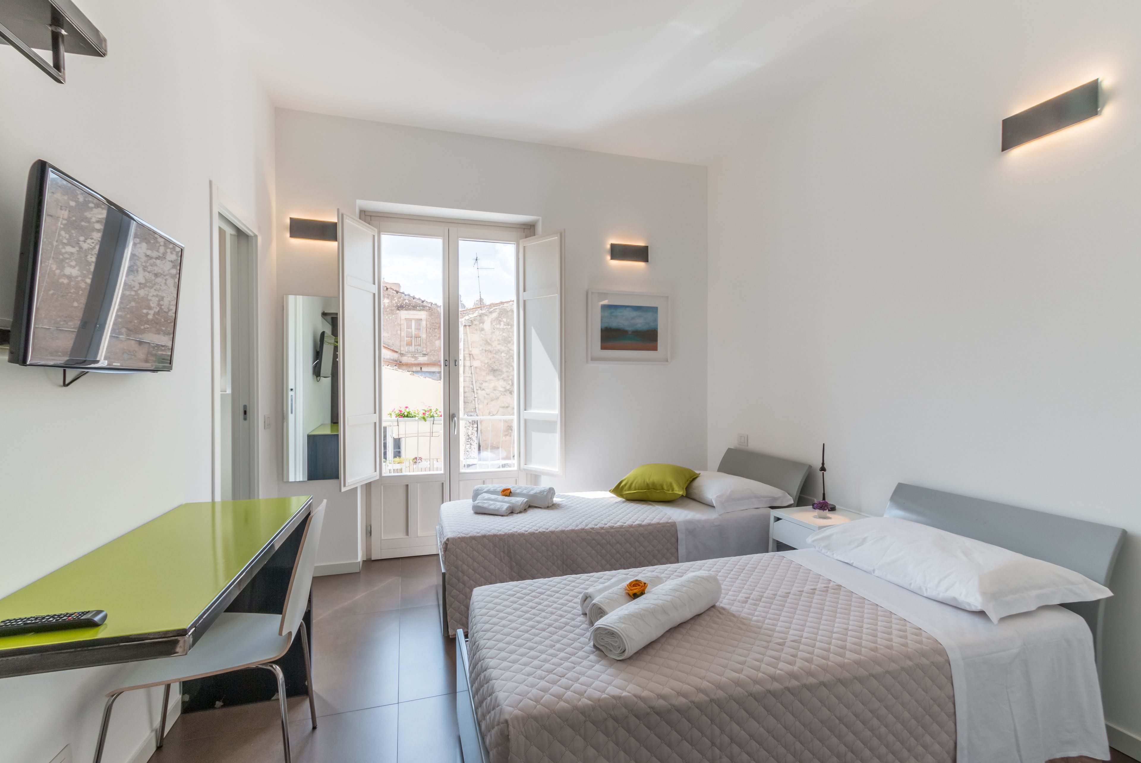 Una camera d'albergo moderna con due letti, una scrivania e un'ampia finestra con vista sulla città.