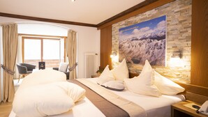 A hotel room with a large bed, a view of the mountains through the window, a stone wall, and a hammock. - Beauty & Wellness Hotel Tirolerhof (Nauders)