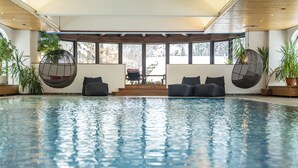 An indoor swimming pool with a seating area, large windows, and potted plants. - Beauty & Wellness Hotel Tirolerhof (Nauders)