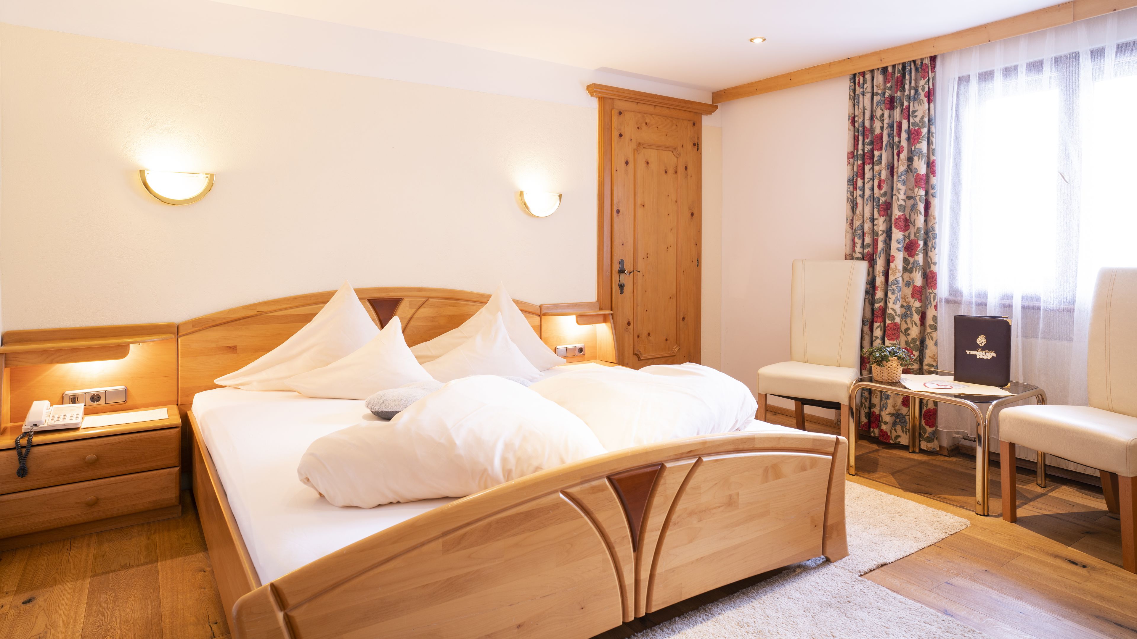 Habitación de hotel ordenada con una cama de madera, lámparas de noche, una silla, un escritorio y un armario.