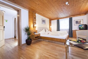 Une chambre d’hôtel moderne avec un plafond en bois, un lit avec une literie blanche, une table de chevet avec une lampe, une plante en pot et un panier de fruits sur la table.