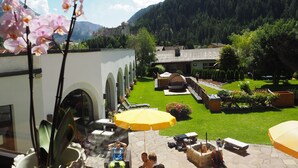 A courtyard with outdoor seating, a fire pit, and a view of a forested mountain. - Beauty & Wellness Hotel Tirolerhof (Nauders)