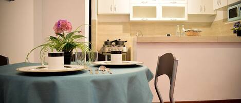 A dining area with a table set for two, a vase with flowers, and a stove in the background.