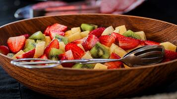 A wooden bowl filled with mixed fruit salad, including strawberries, kiwi, and pineapple, with a spoon in it.
