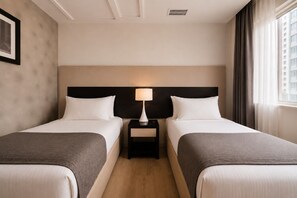 Habitación de hotel con dos camas, una mesita de noche con lámpara, un cuadro en la pared y una ventana con cortinas.