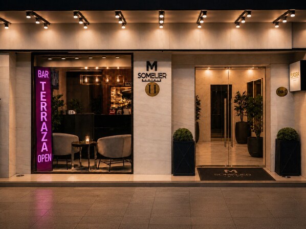 Una entrada de hotel moderna con un bar llamado 'BAR TERAZA OPEN' y un letrero que dice 'M SOMELIER HOTEL'.
