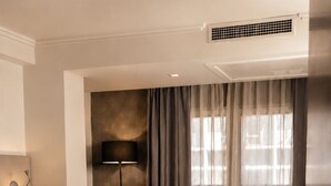 A hotel room with a bed, a sofa, a desk with a lamp, and a wall-mounted air vent. - Hotel Sommelier Agustinas (Santiago)