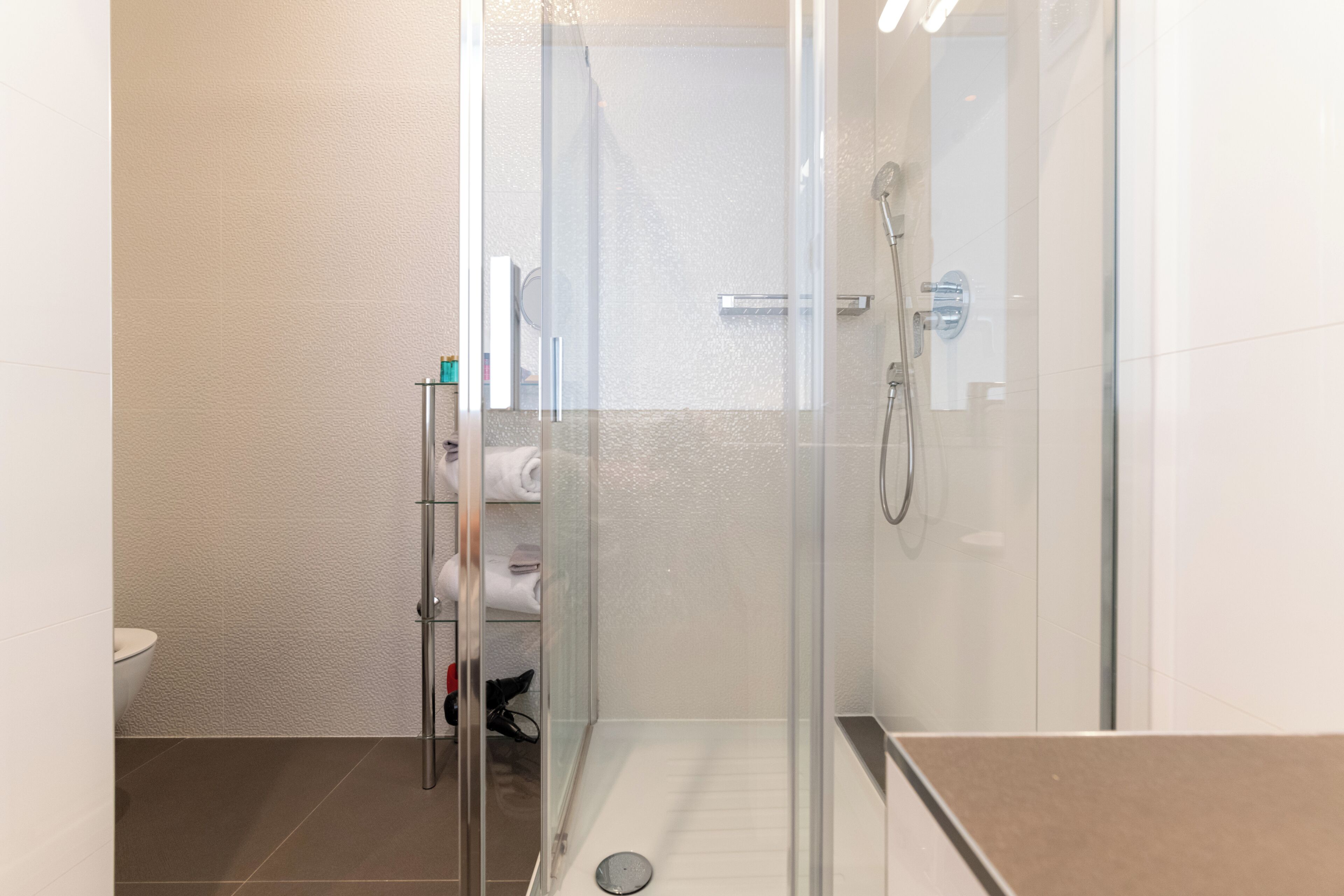 Un baño moderno con ducha envuelta en vidrio, inodoro y toallero con toallas dobladas.