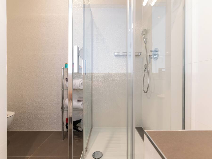 Un baño moderno con ducha envuelta en vidrio, inodoro y toallero con toallas dobladas.
