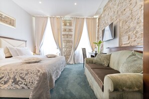 Habitación de hotel con una cama grande, un sofá, un televisor montado en una pared de piedra y un escritorio con una planta.