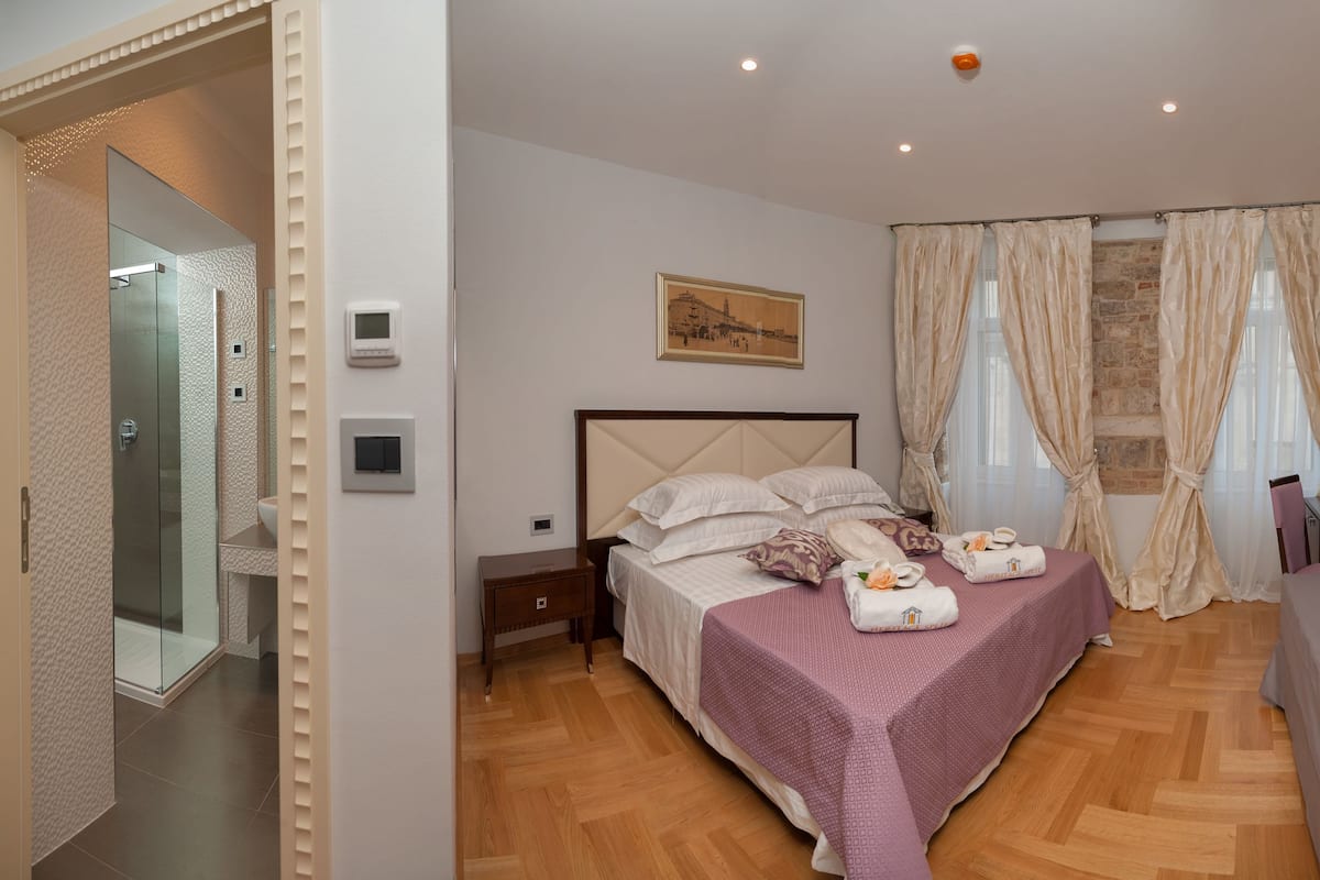 A bedroom with a bed, a bedside table, a TV mounted on the wall, and a shower area.