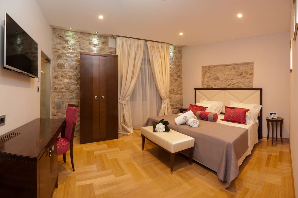 A hotel room with a bed, a bench, a TV, a wardrobe, and a stone wall.