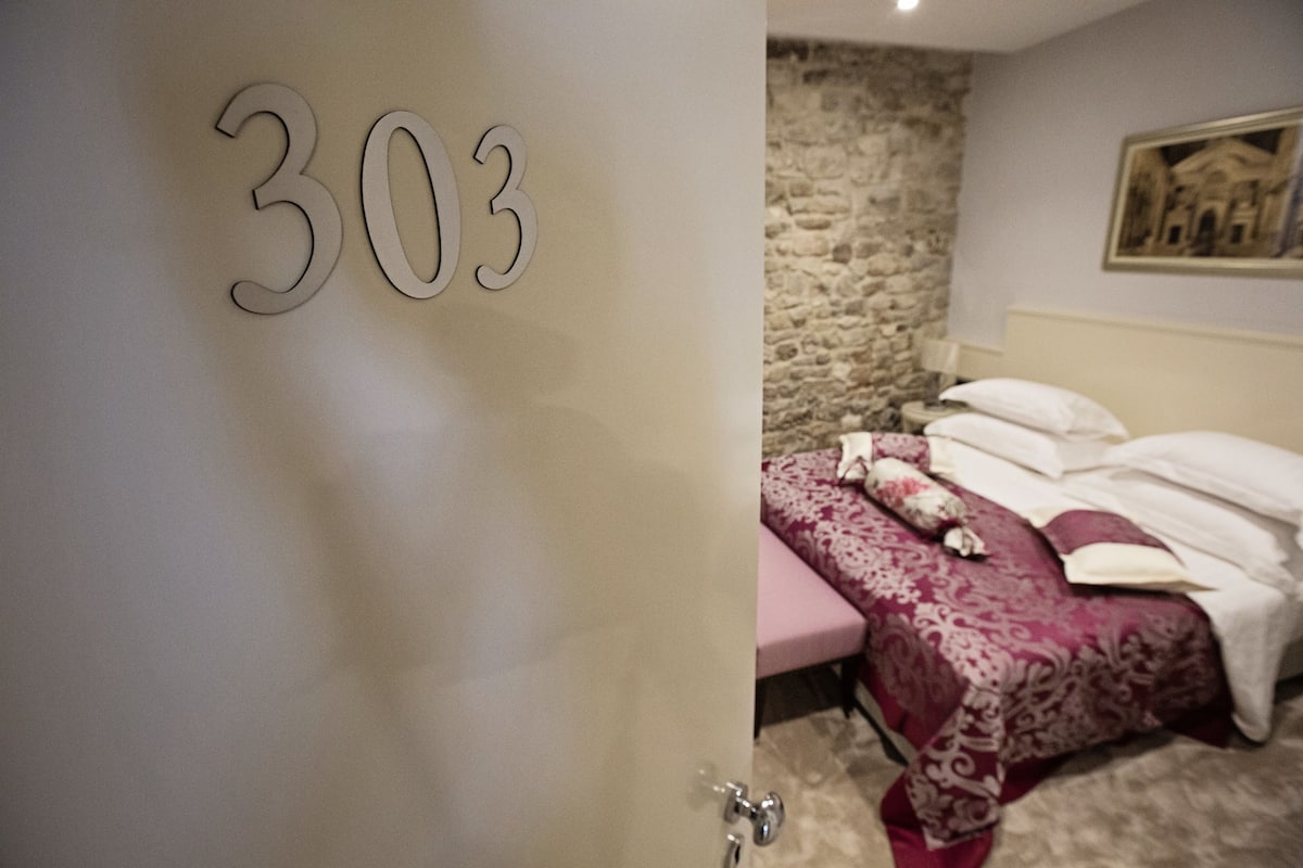 A room with a bed, a stone wall, and a number '303' on the door.