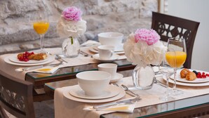 Un ambiente de desayuno con pared de piedra, vajilla blanca y arreglos florales.