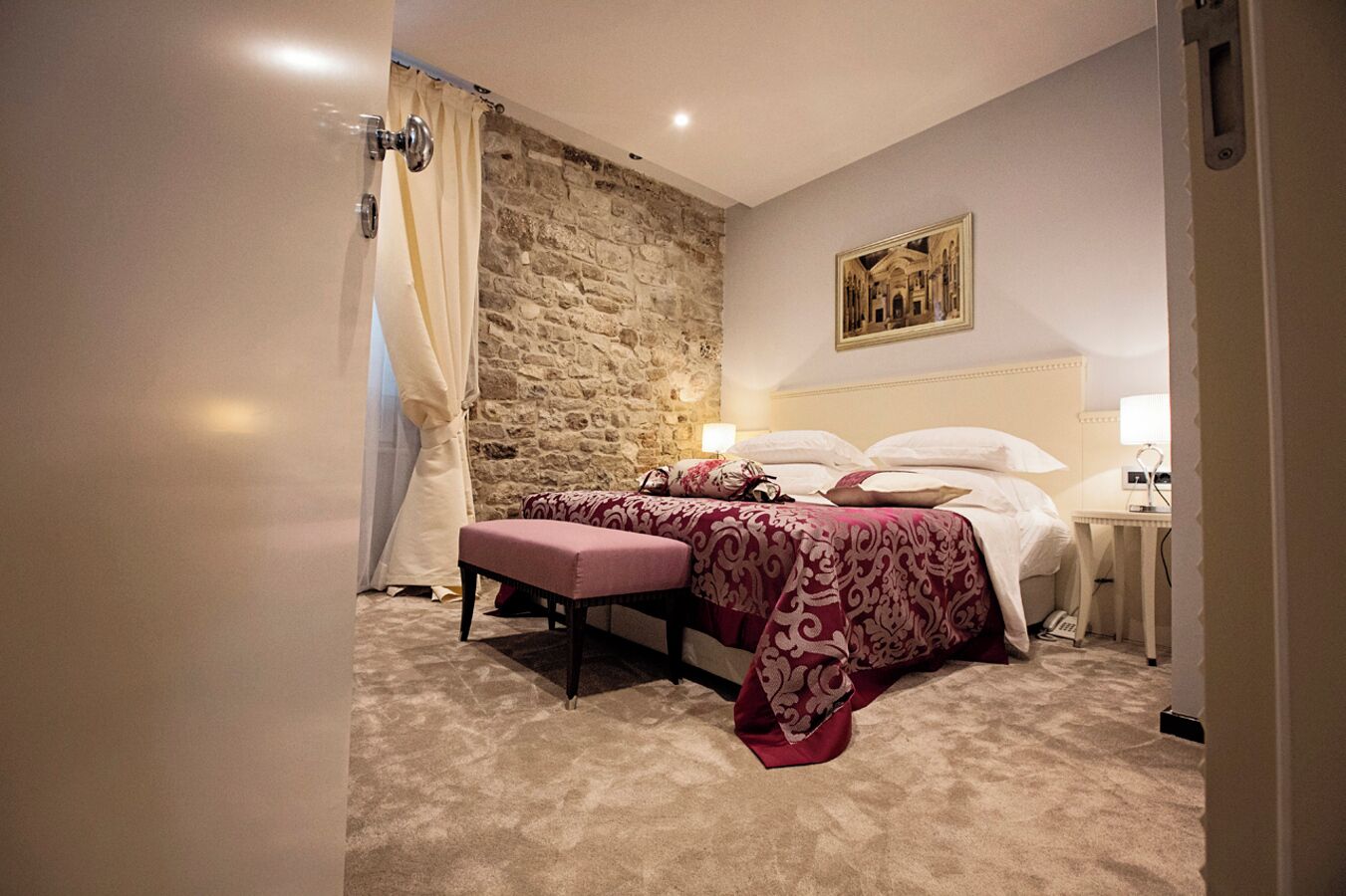 Ein Schlafzimmer mit Steinwand, einem Bett mit gemustertem Überwurf, einem Nachttisch mit Lampe und einem Fenster mit Vorhängen.