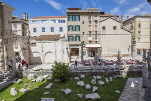 A courtyard with stone ruins, outdoor seating, and historic buildings with multiple stories and balconies.