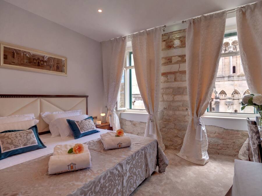 A hotel room with a large bed, a view of a historic building, and a stone wall.