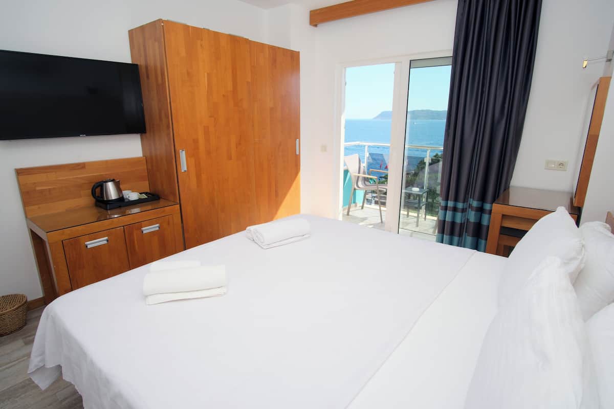 Ein Hotelzimmer mit Bett, Holzschrank, Flachbildfernseher, Kaffeemaschine und Meerblick durch eine Schiebetür.