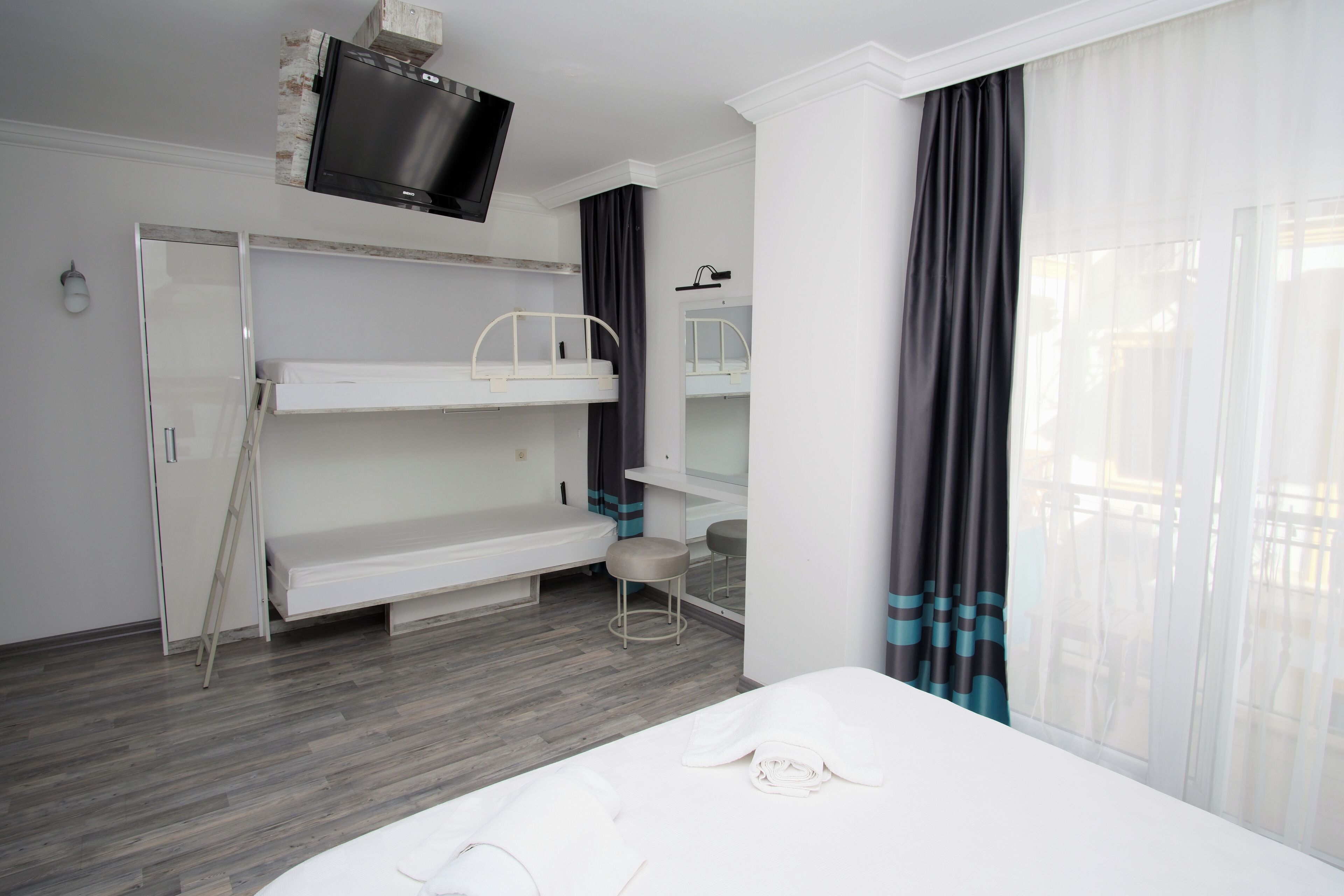 A hotel room with bunk beds, a television, a desk, and a window with curtains.