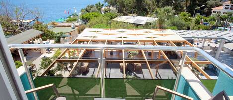 A rooftop terrace with a view of the sea, surrounded by greenery and buildings.