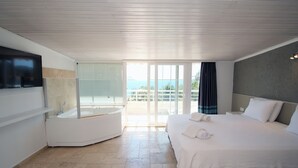 Quarto de hotel moderno com cama grande, banheira integrada e varanda com vista para o mar.