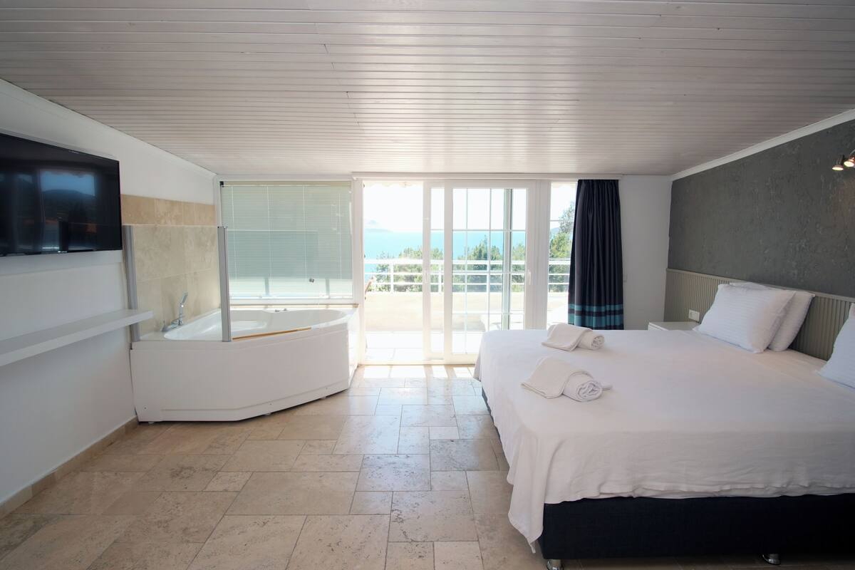 Ein modernes Hotelzimmer mit einem großen Bett, einer integrierten Badewanne und einem Balkon mit Meerblick.