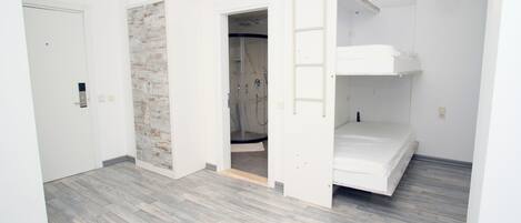 Una habitación con literas, zona de ducha y una puerta que da a otra habitación.