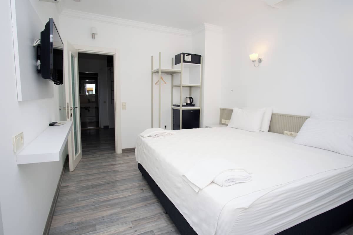 Ein Hotelzimmer mit einem großen Bett, einem an der Wand befestigten Fernseher, einem Kleiderschrank und einer kleinen Ablagefläche mit einem Wasserkocher.