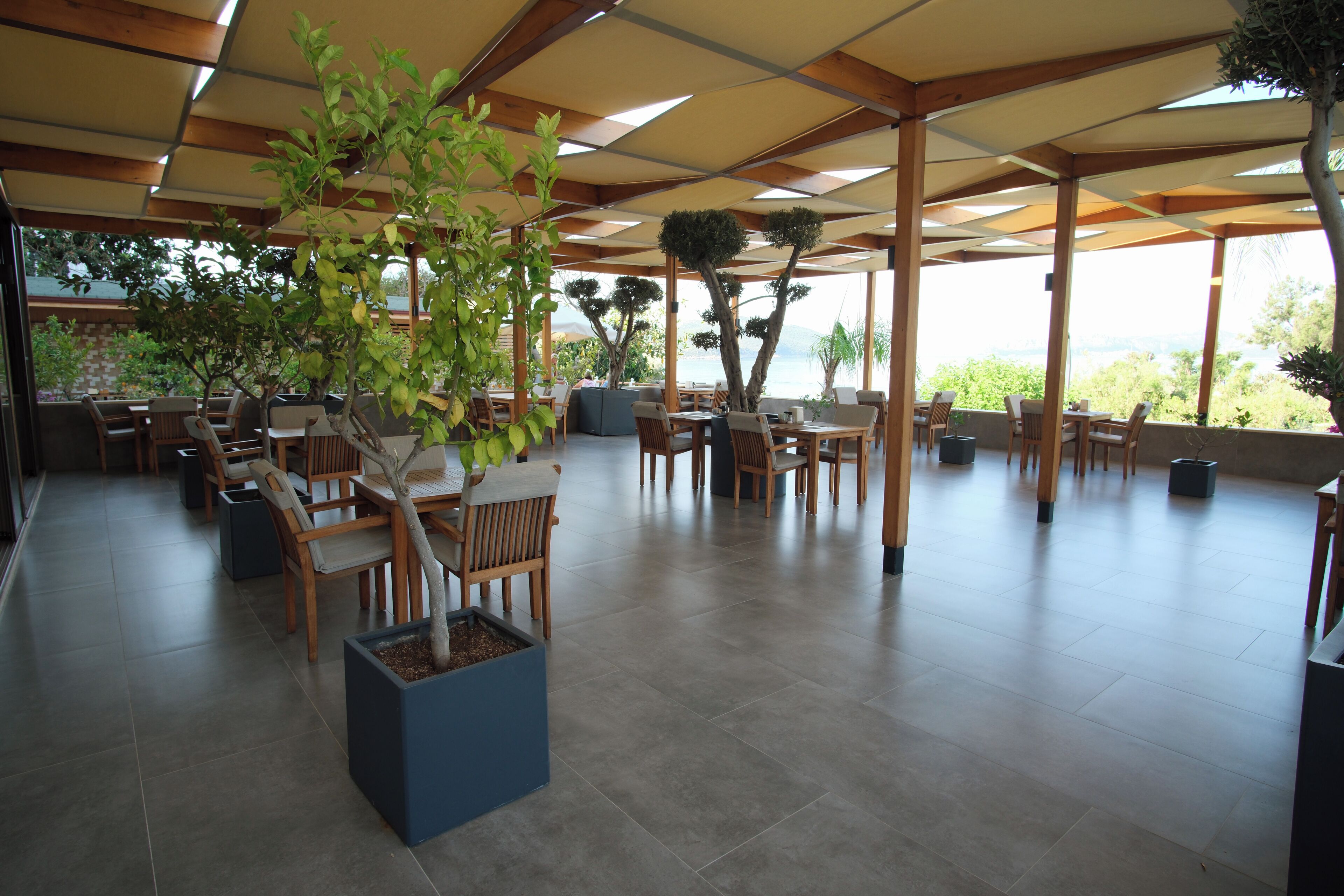 Un espace extérieur aménagé en terrasse, avec des tables et des chaises en bois, des plantes en pot et une vue sur la mer.