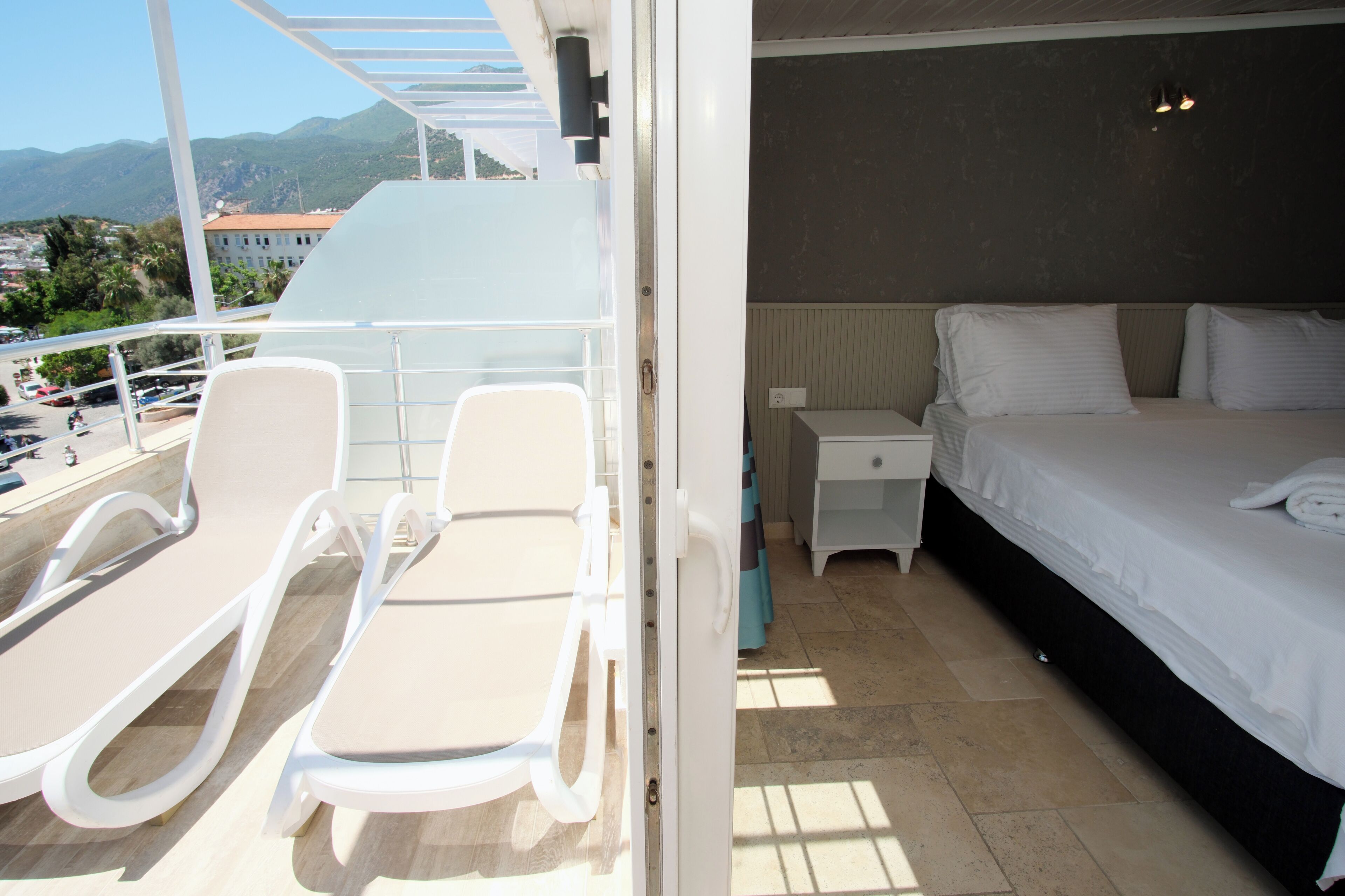 Ein Balkon mit weißen Liegestühlen und einem Bett mit weißer Bettwäsche.